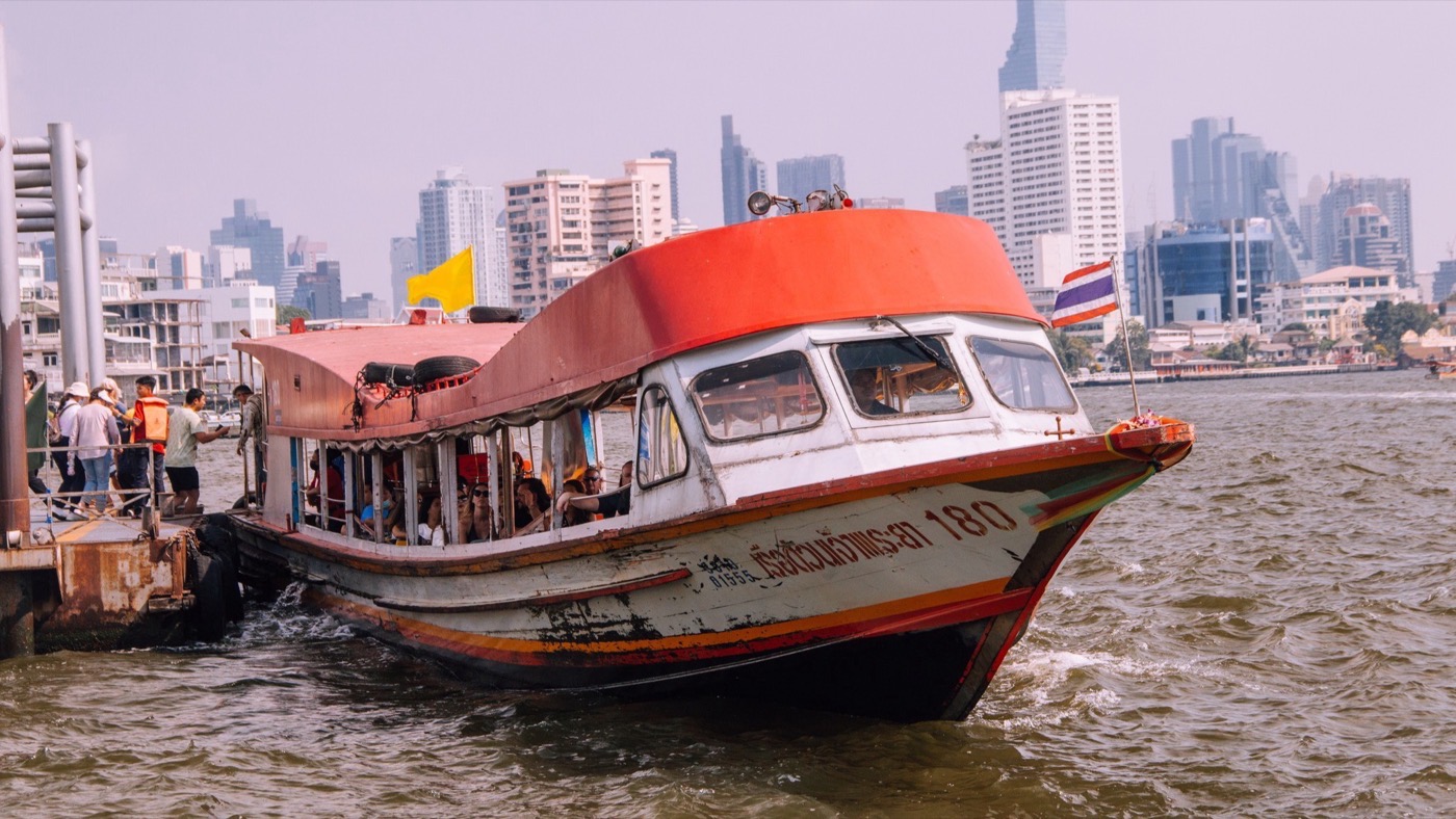 Un barco del Chao Phraya con bandera amarilla en un embarcadero de Bangkok